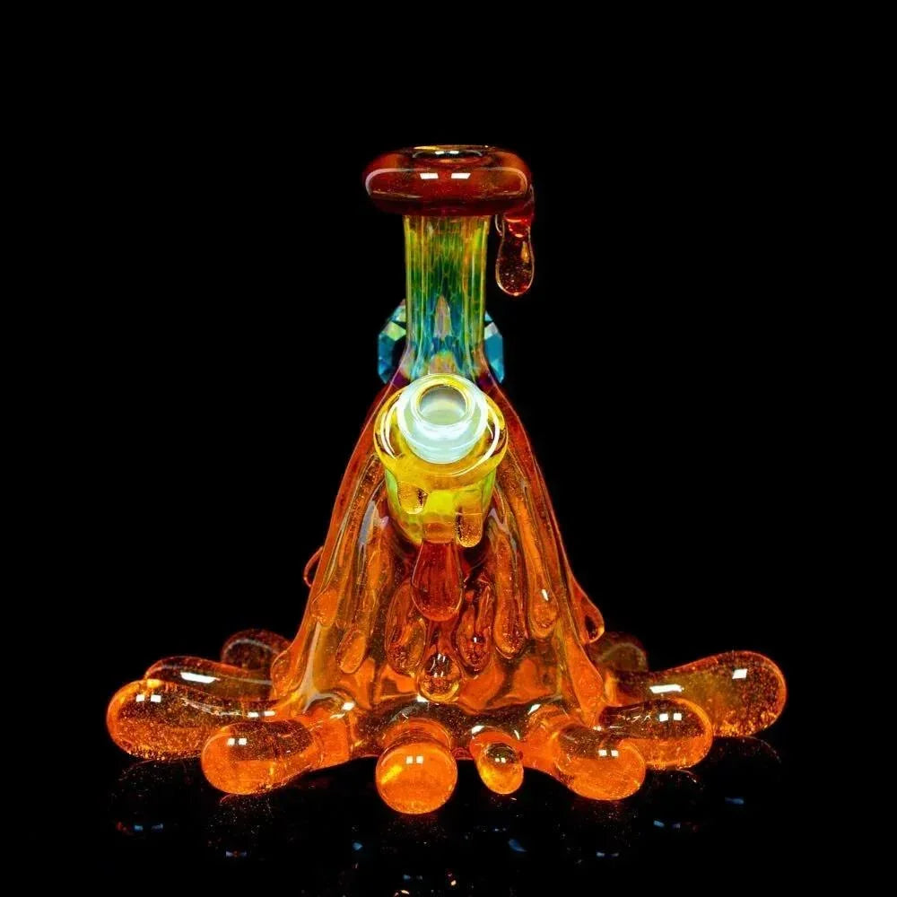 Heady glass dab rig with orange dripping design and matching cap on black background