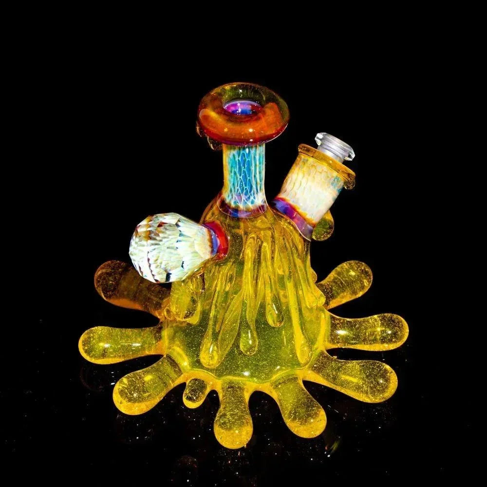 Hand-blown yellow glass dab rig with splash design and colorful matching cap on black background
