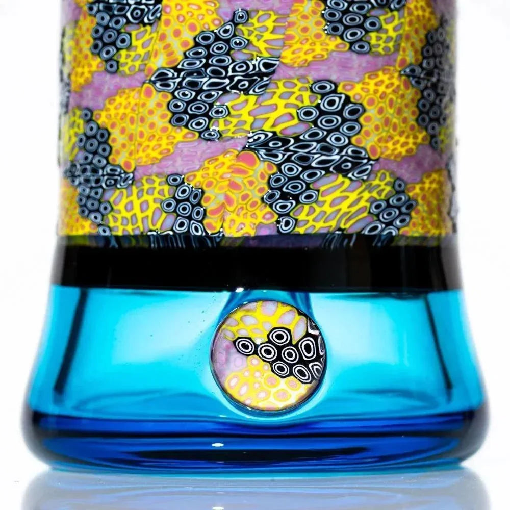 Close-up of a blue glass rig with vibrant yellow, pink, and black murrine patterns