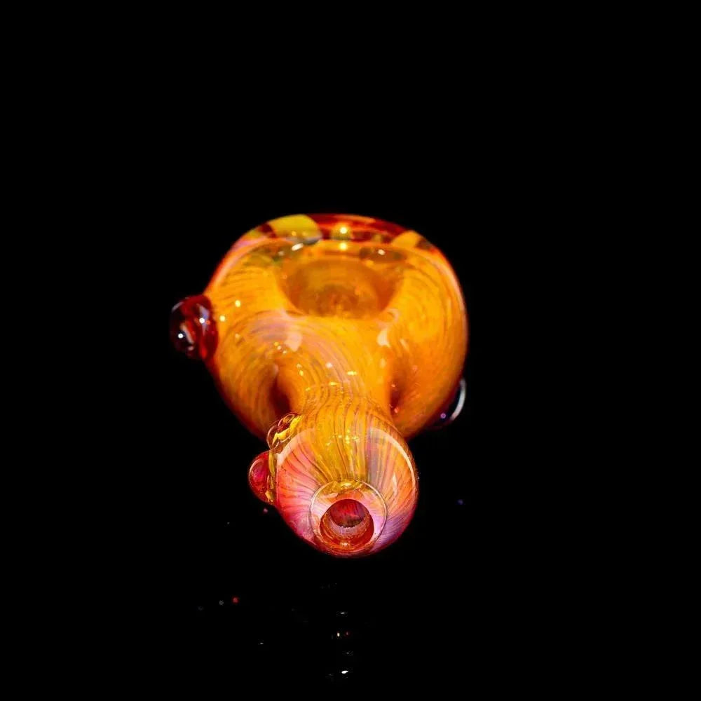 Gold fume glass spoon pipe with orange and yellow swirls on black background