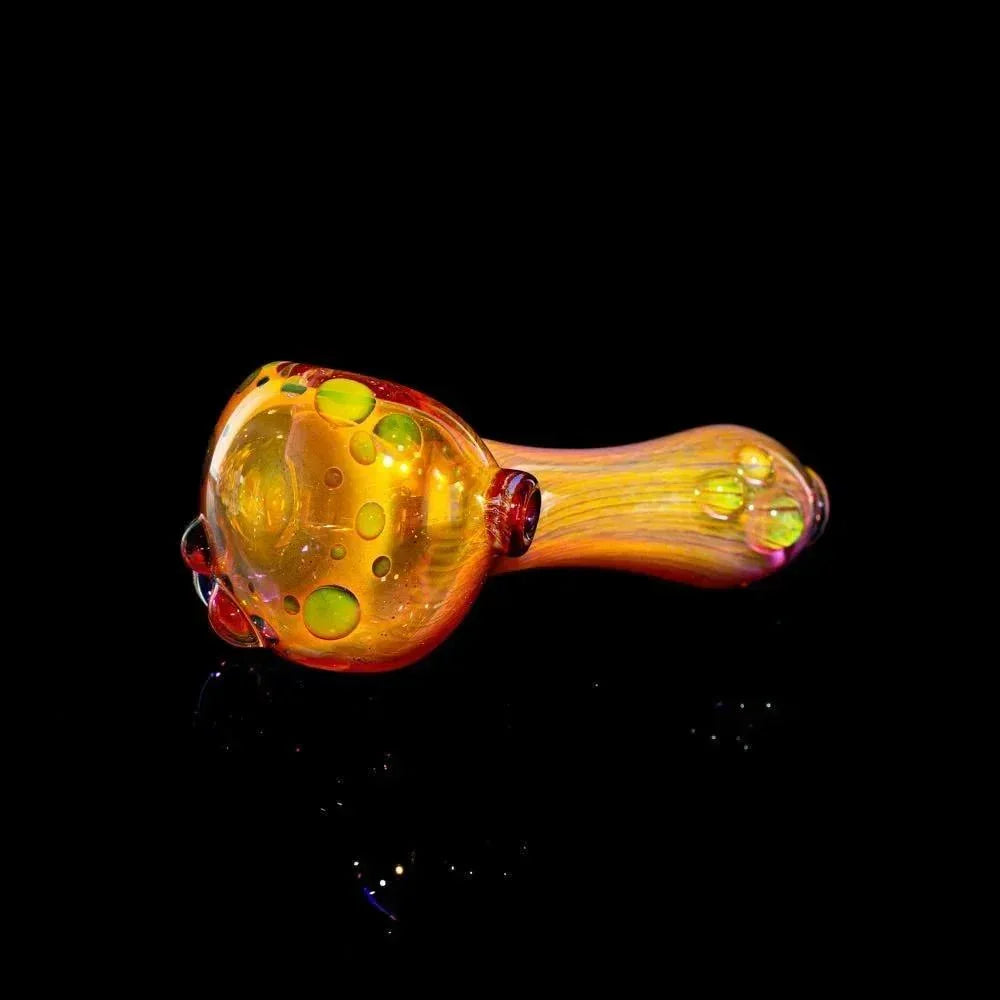 Gold fumed glass spoon pipe with yellow and green bubbles on a black background