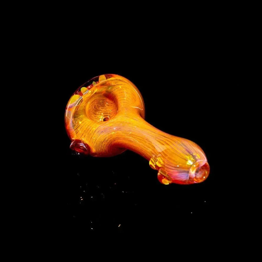 Gold fumed glass spoon pipe with vibrant color accents on a black background.