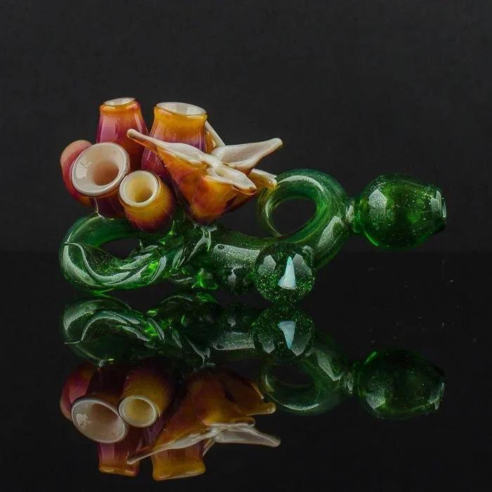 Artistic glass pipe with floral design, vibrant green stem, and amber accents on reflective surface