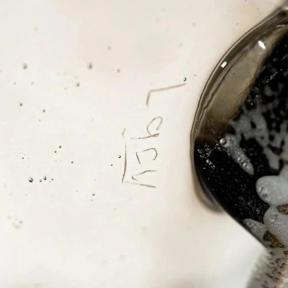 Close-up of artist signature etched on clear glass art piece with dark accent detail