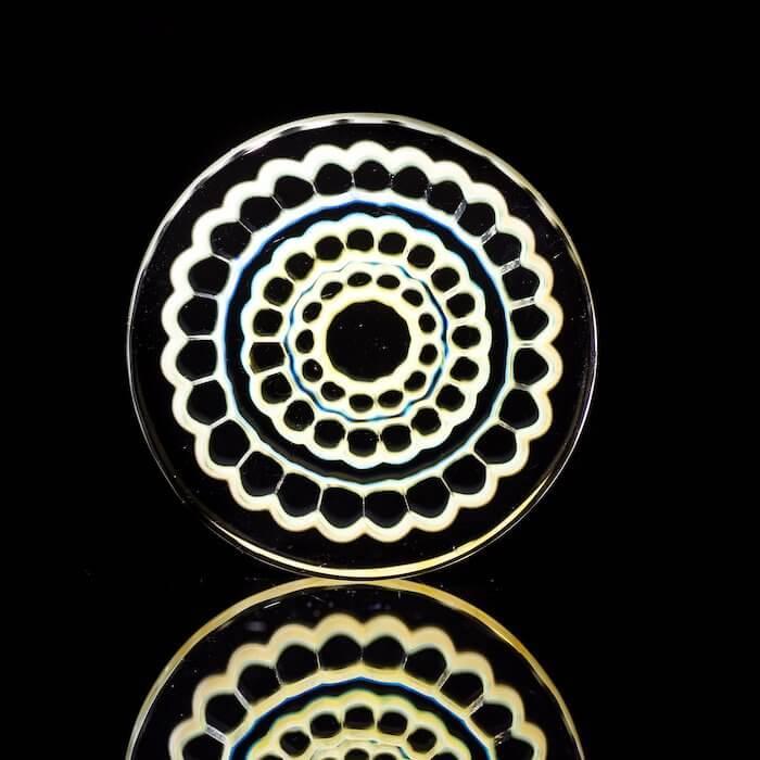 Intricate heady glass disc with concentric honeycomb patterns, glowing against black background