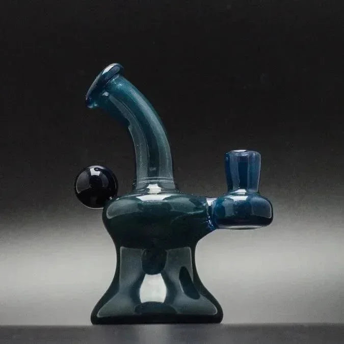 Teal glass dab rig with curved neck and side carb cap, studio-lit for heady glass collection