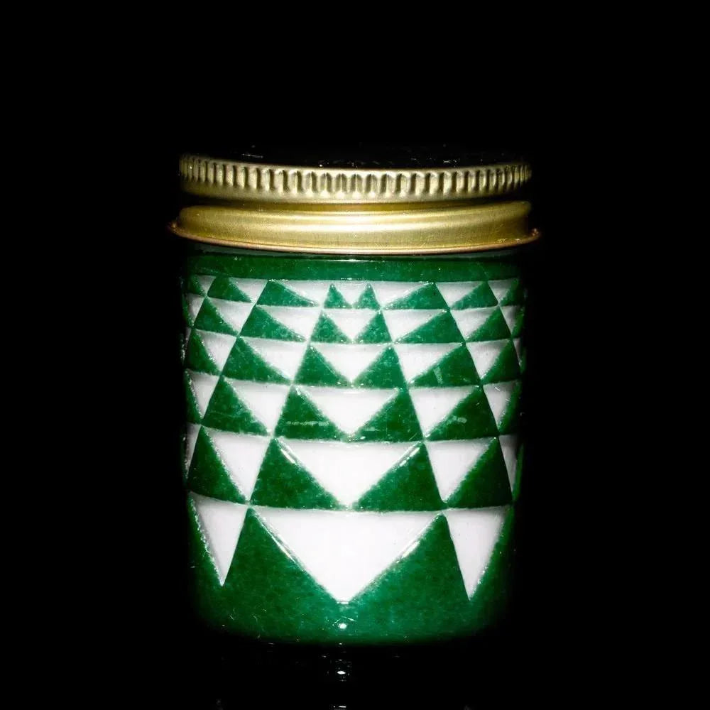 Green glass jar with geometric white triangle pattern and gold metal lid on black background.