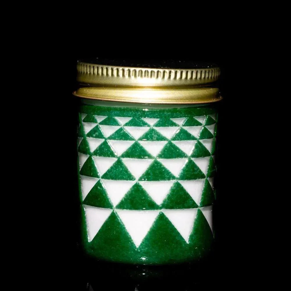 Green glass jar with white triangle pattern and gold lid on black background