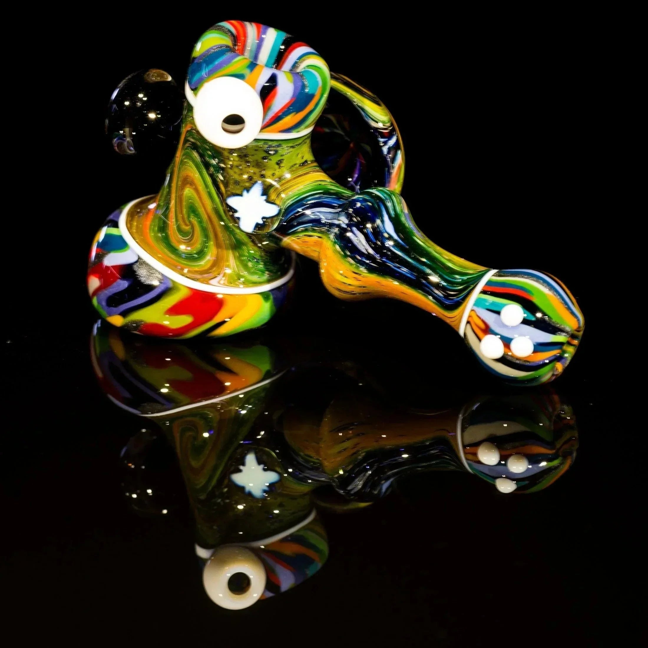 Colorful heady glass pipe with swirls, eyes, and flower design on black reflective surface