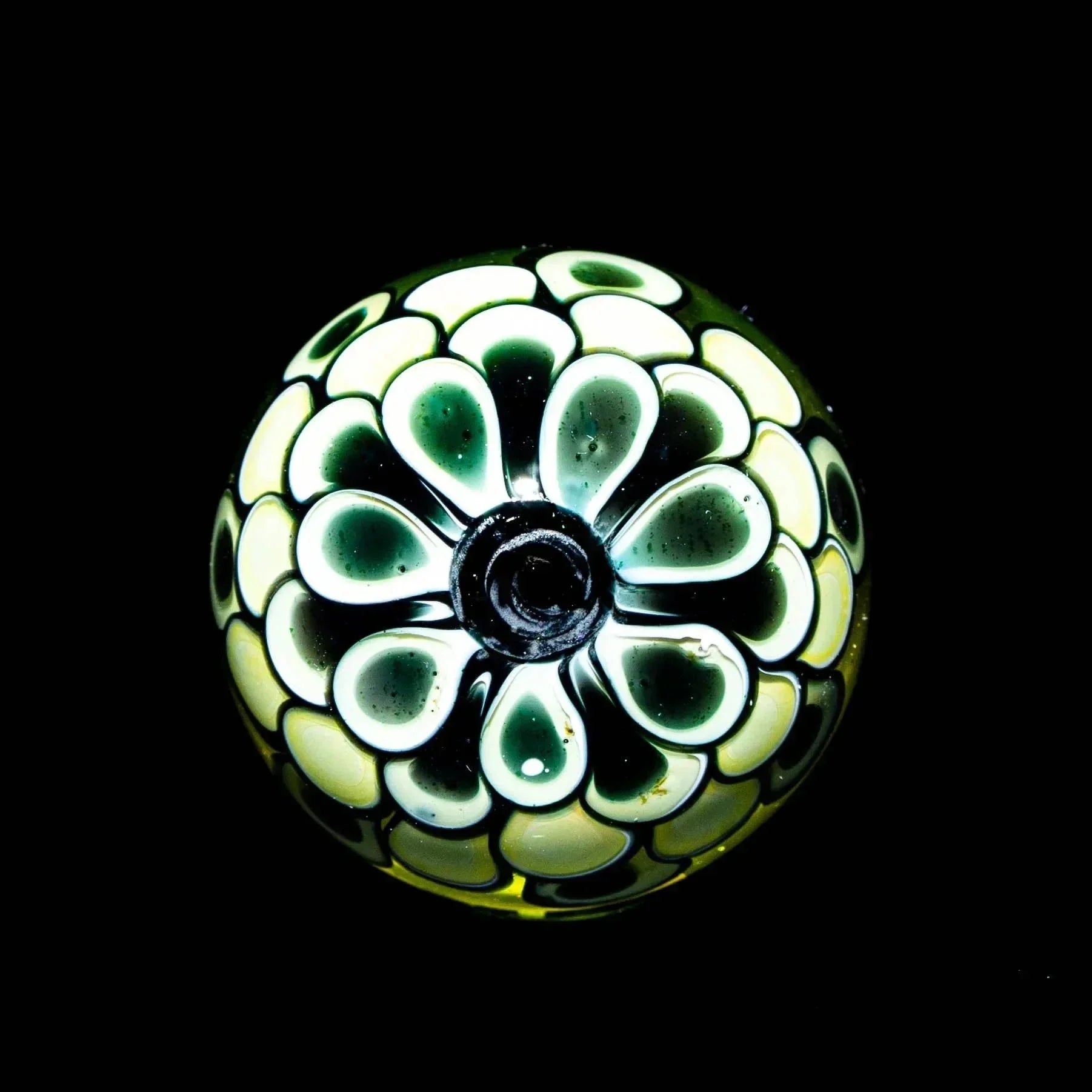 Hand-blown glass marble with intricate green and yellow petal design on a black background