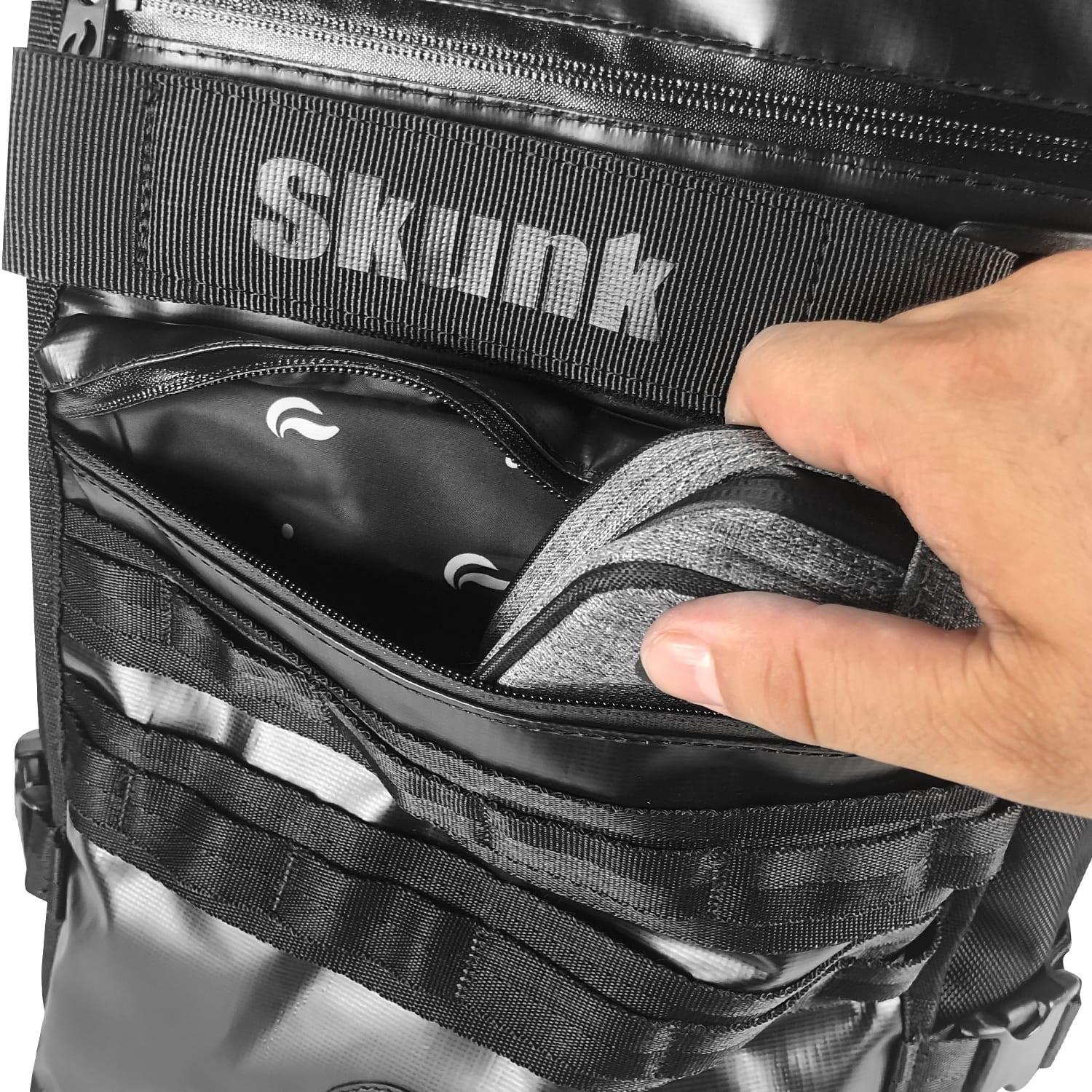 Hand placing item in black Skunk bag front pocket with visible zipper and gray inserts