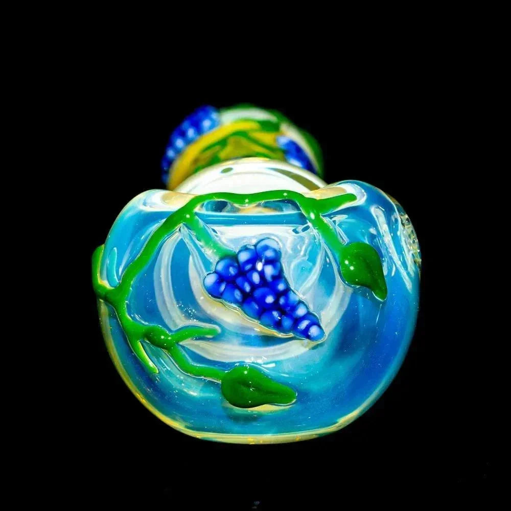 Hand-blown glass spoon with blue flower and green leaf details on a dark background.