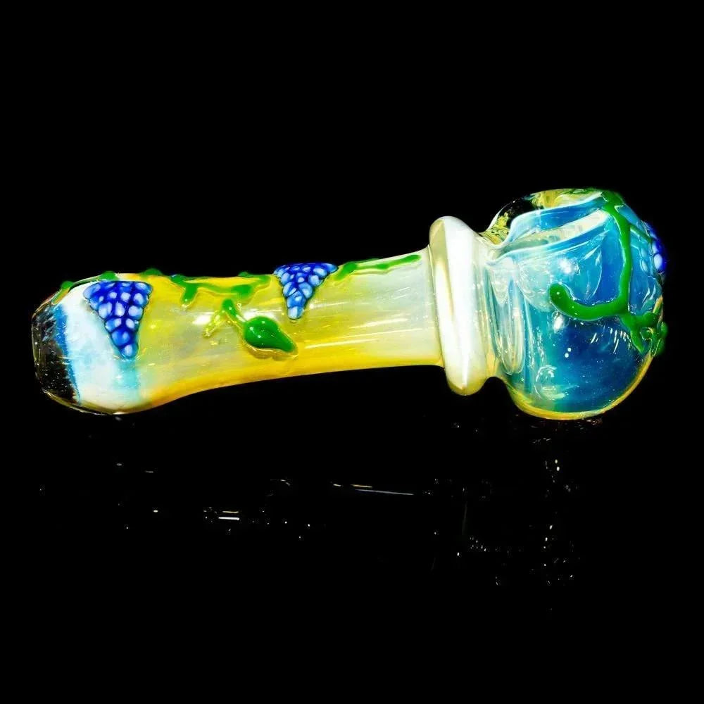 Hand-blown glass pipe with blue grape vine design on a yellow and clear body, against black background.