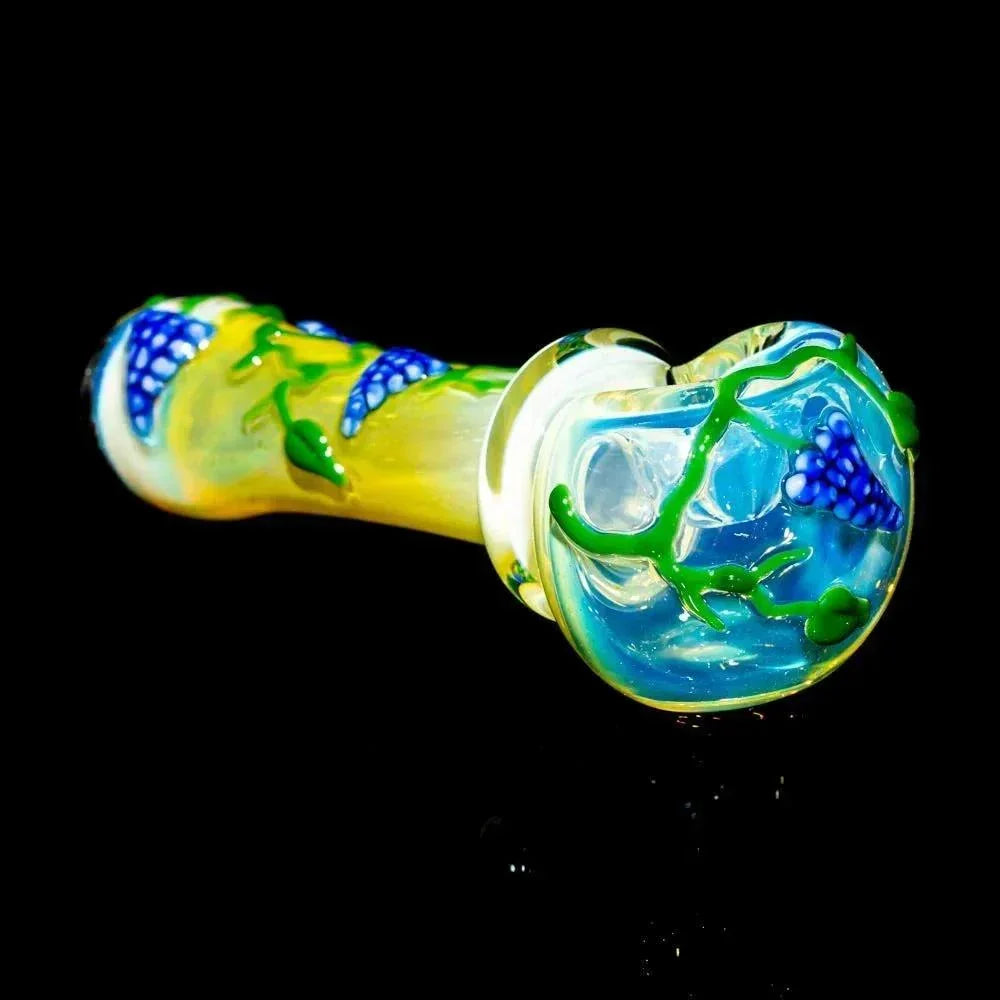 Hand-blown glass spoon pipe with blue flower and green vine accents on a yellow body