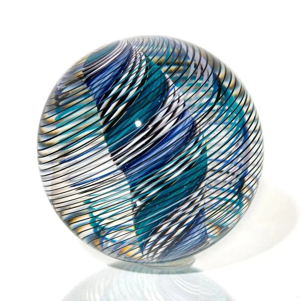 Handcrafted glass marble with blue, green, and white linework design on white background