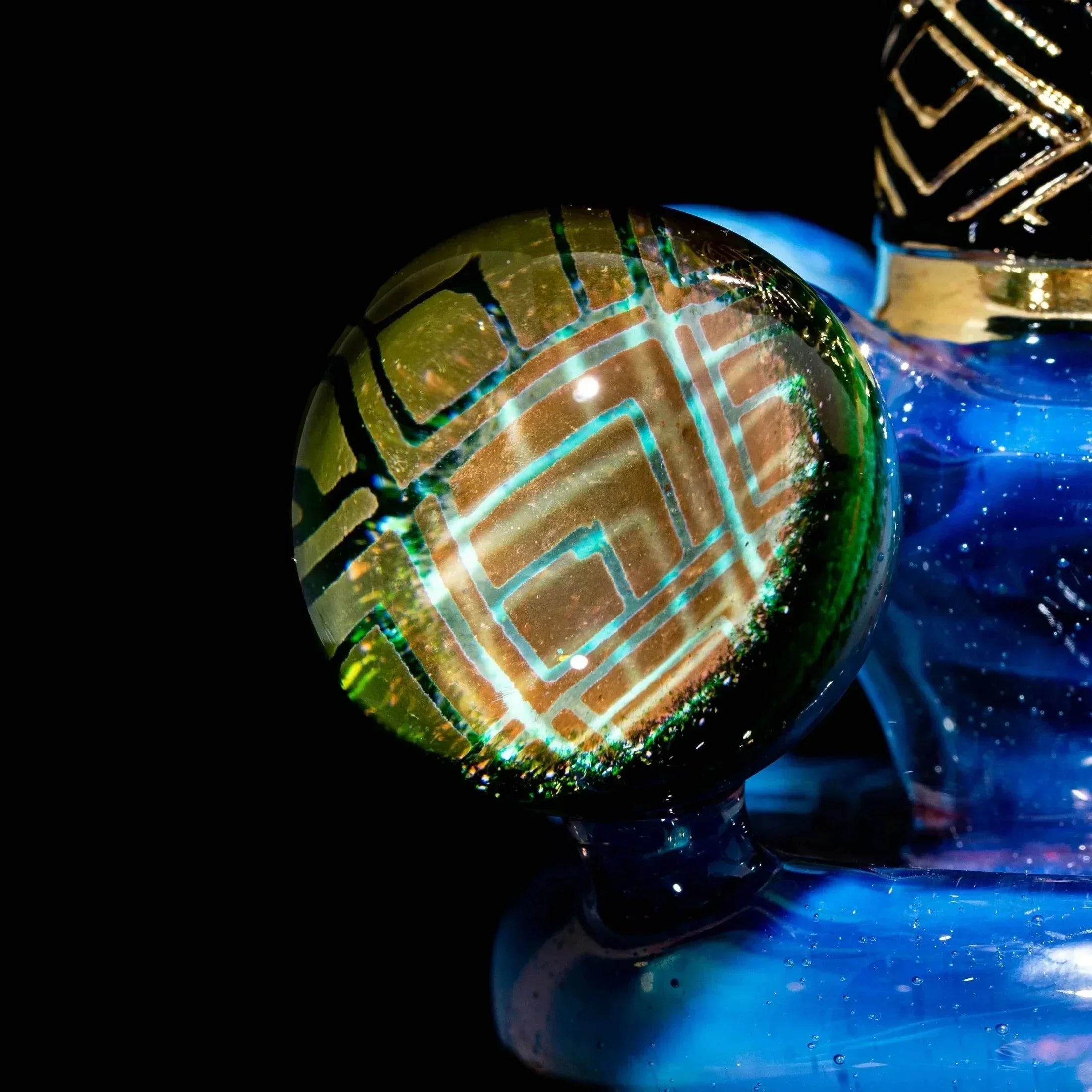 Close-up of blue glass art piece with gold geometric deco accents and green marble