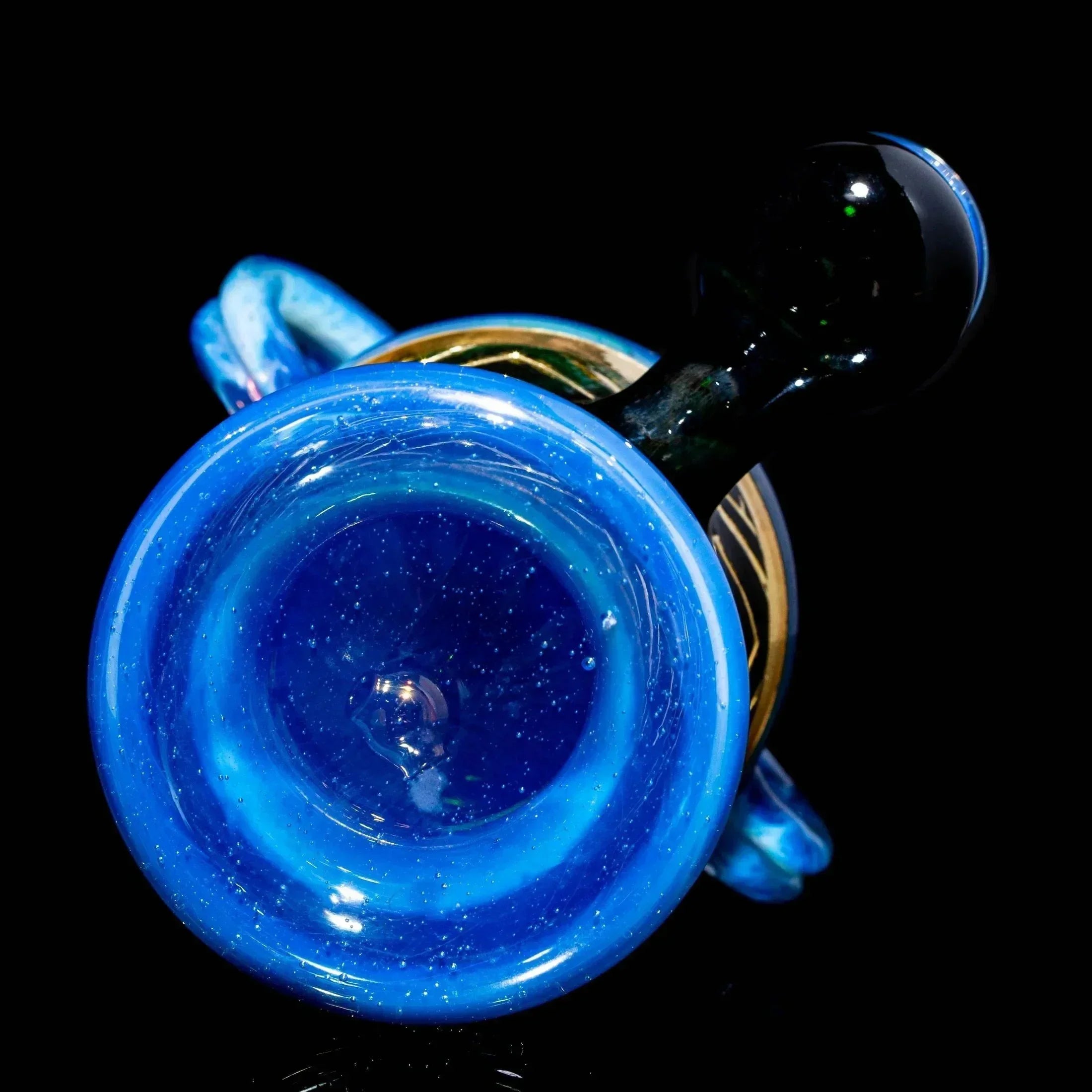 Blue art glass vessel with swirling accents and decorative handle, displayed on black background.