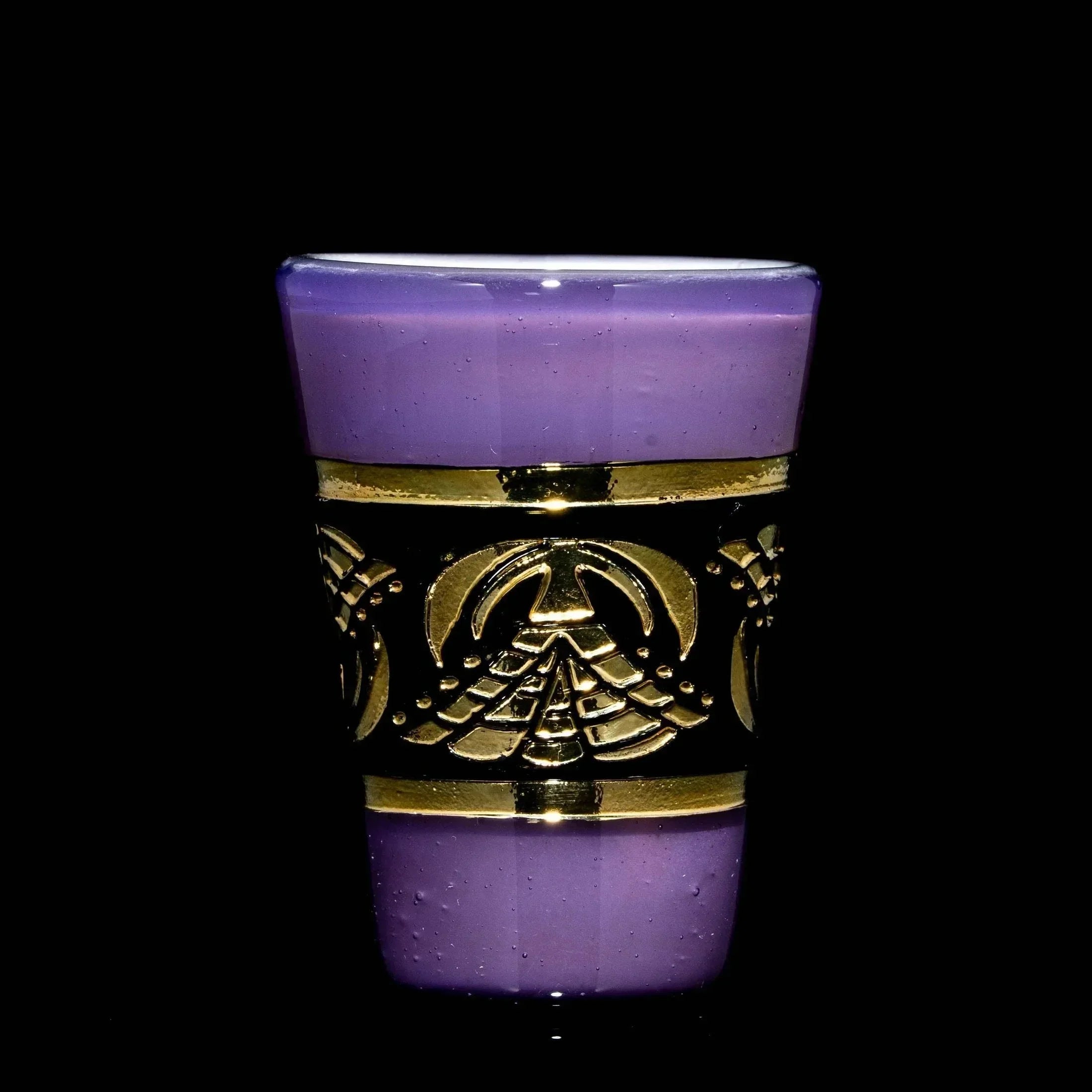 Purple satin glass shot glass with decorative gold band and geometric pattern on black background