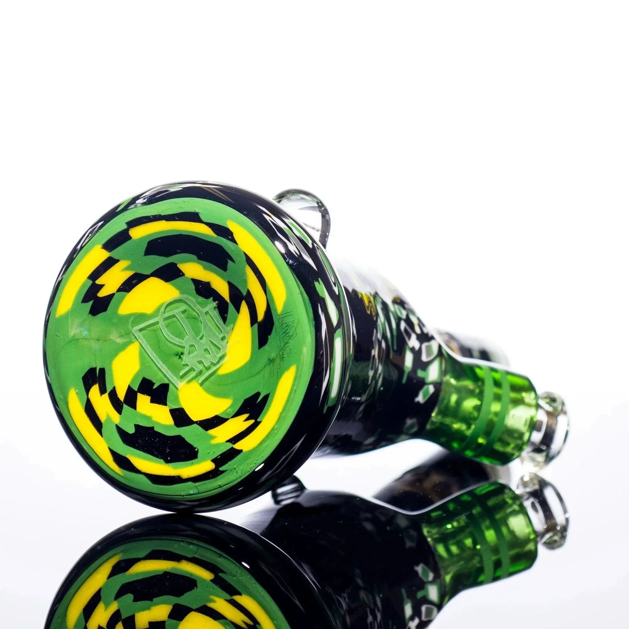 Vibrant green, yellow, and black swirl glass pipe with etched logo, reflecting on glossy surface