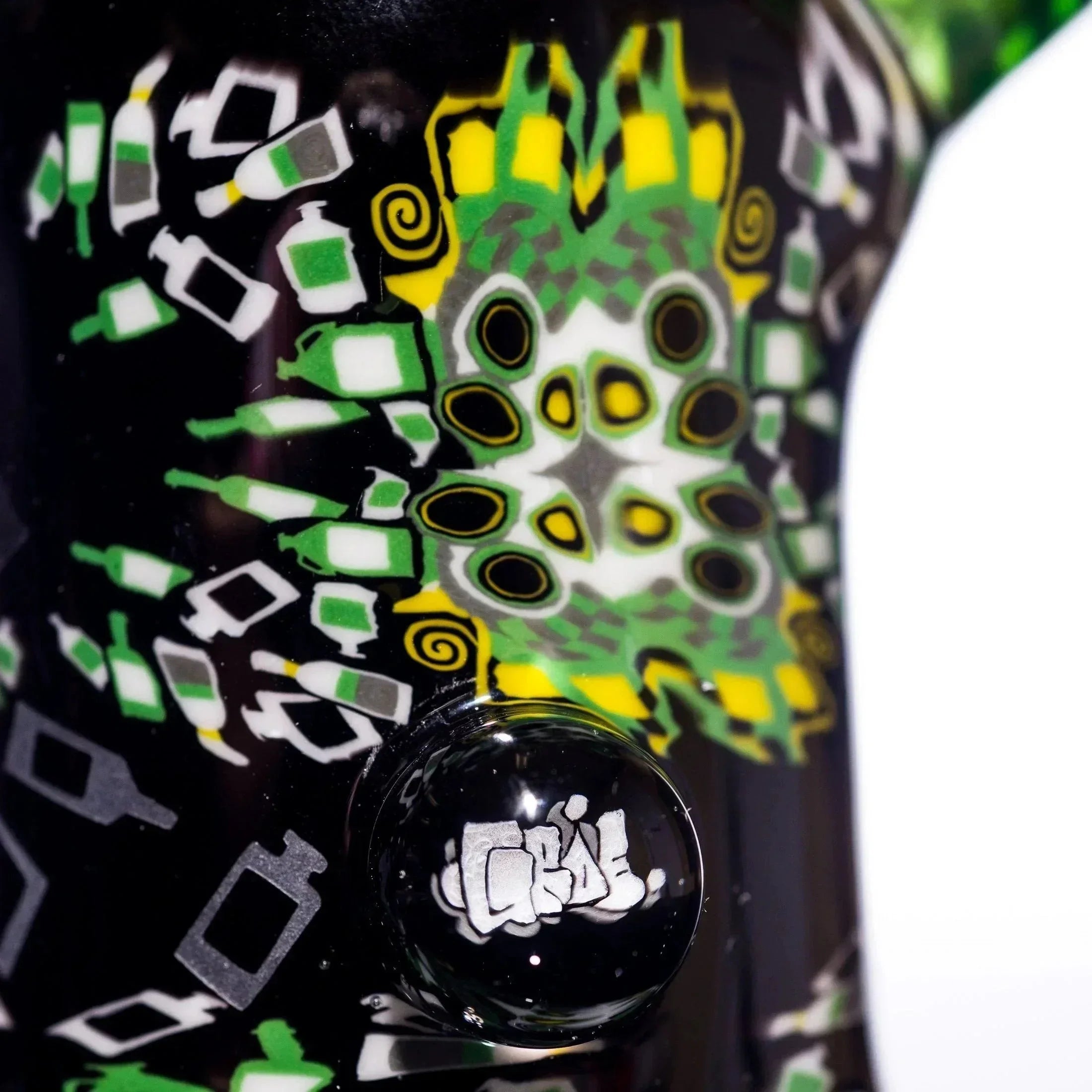 Heady glass pipe with vibrant green, yellow, and white bottle patterns on black base, featuring a signed glass bubble.
