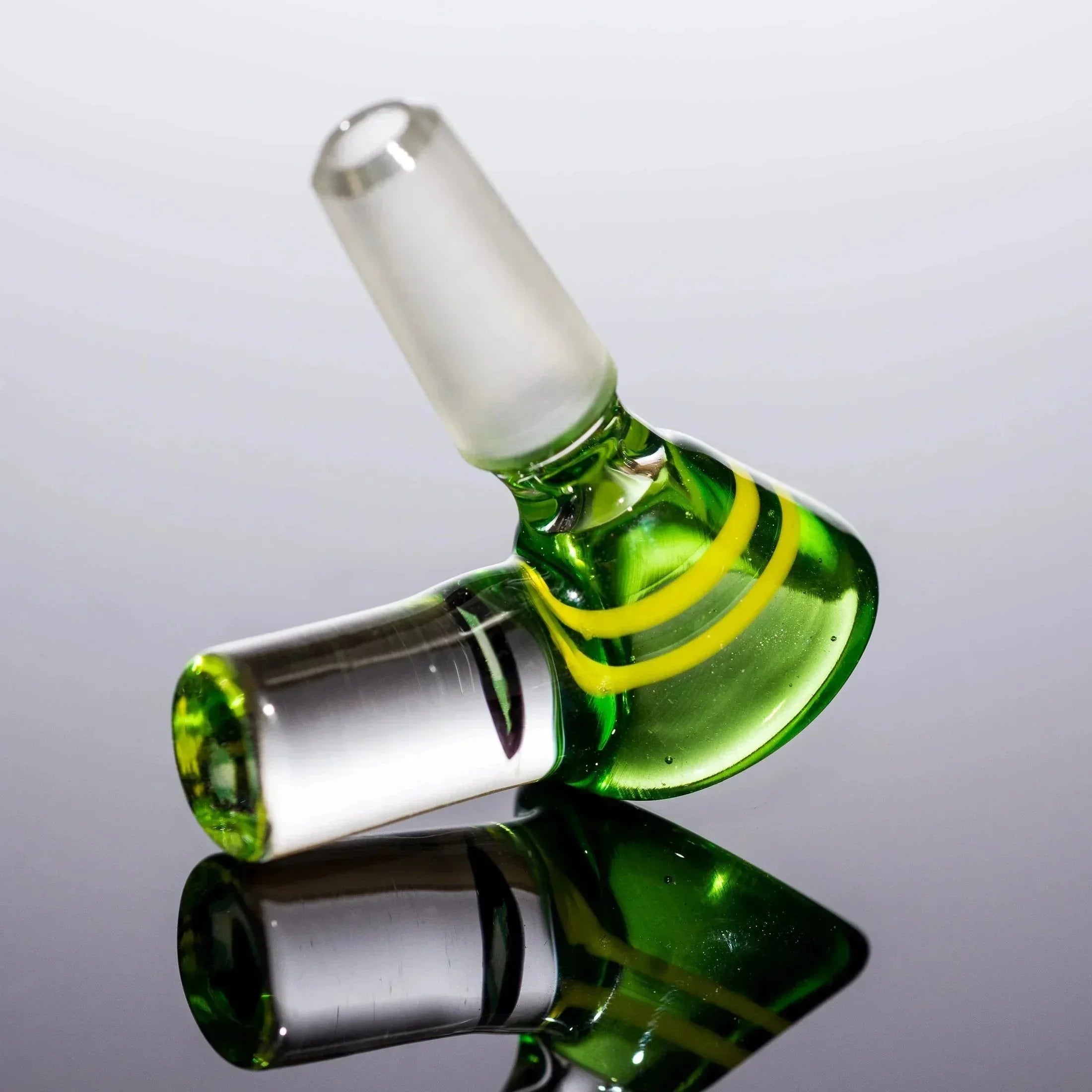 Green glass bong bowl with yellow swirls and clear stem, reflective surface