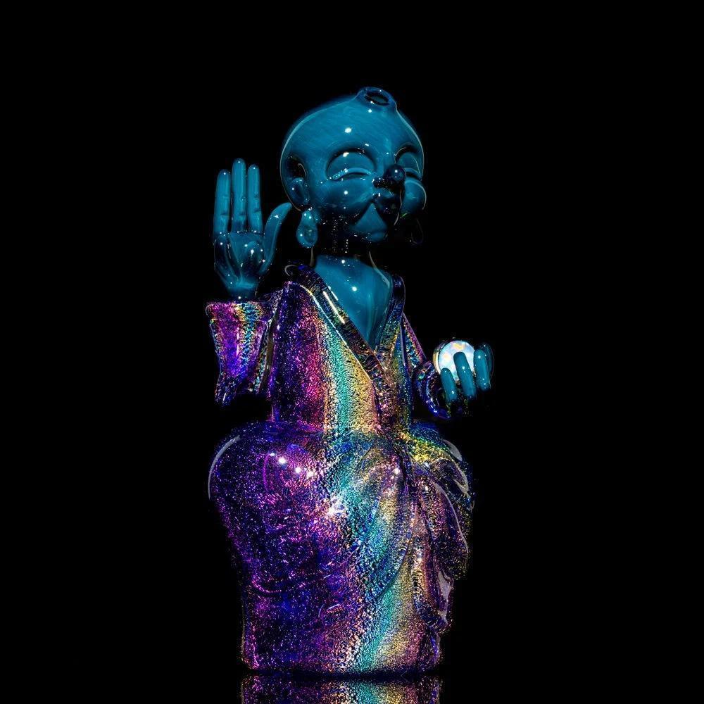 Colorful glass Buddha figurine with iridescent robe, hand raised, against black background