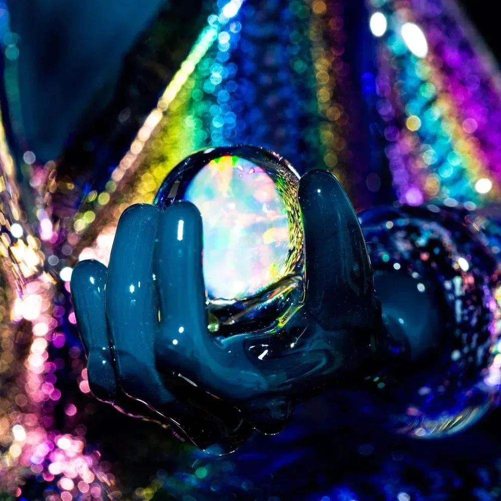 Close-up of iridescent glass sculpture hand holding opalescent marble with colorful lights