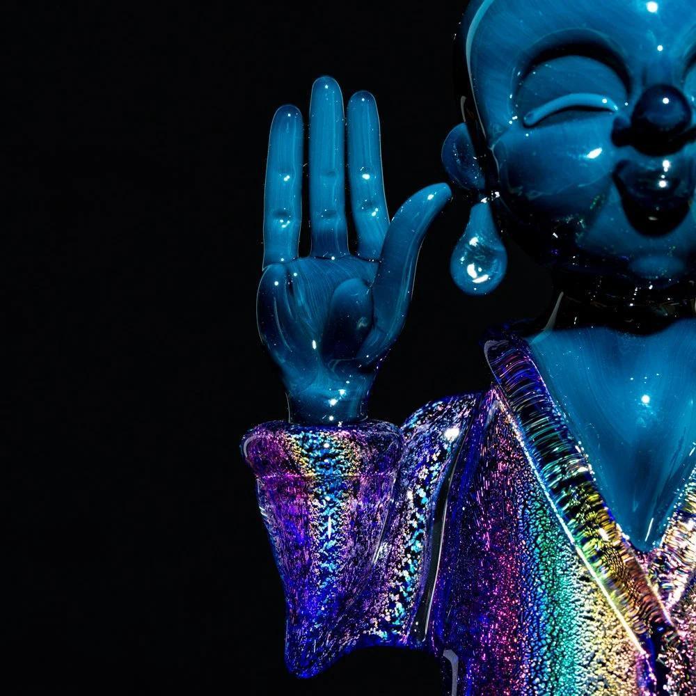 Iridescent Buddha-inspired glass art sculpture with vibrant colors on a dark background