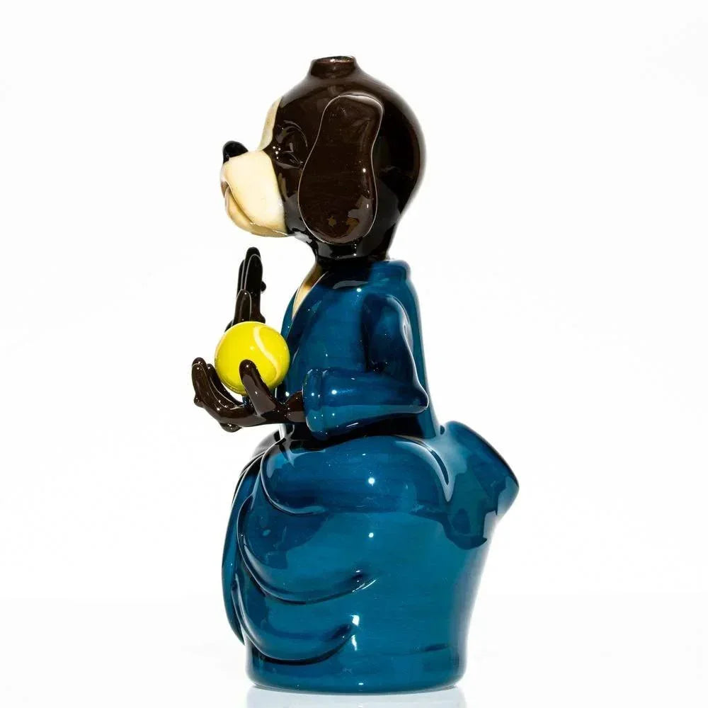 Hand-blown glass dog figure meditating in blue robe holding yellow ball, side view