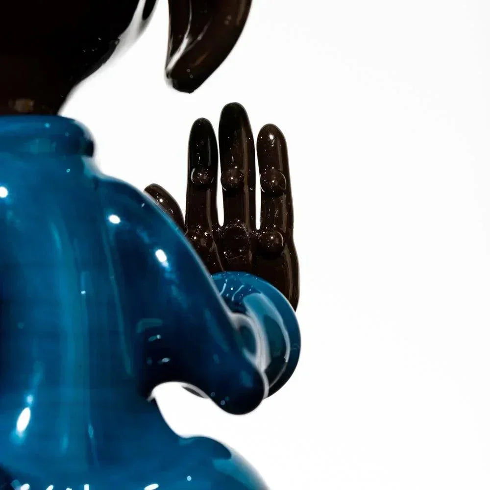 Close-up of a glass dog sculpture in a meditative pose, blue body with raised hand