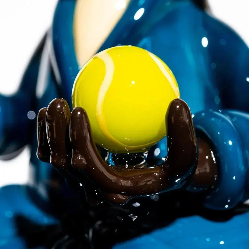 Handcrafted glass sculpture of a dog paw holding a yellow tennis ball, detailed close-up.