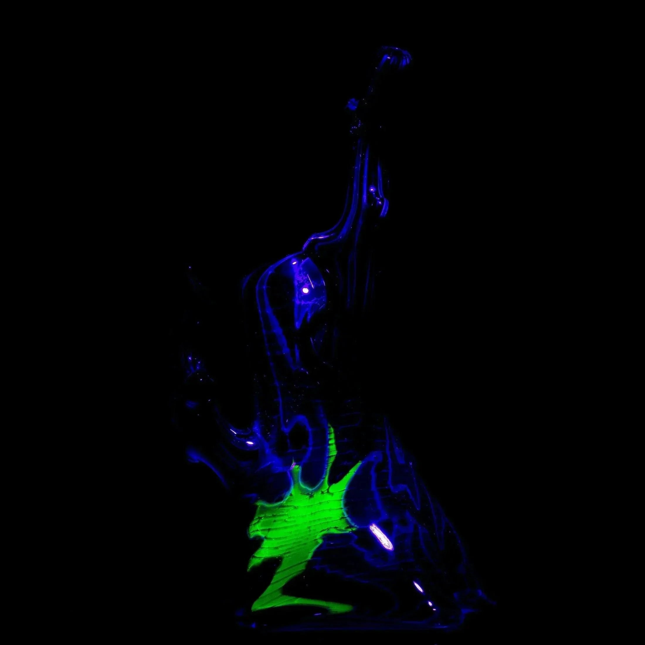 Artistic glass water pipe with glowing neon green and blue accents in a dark setting.