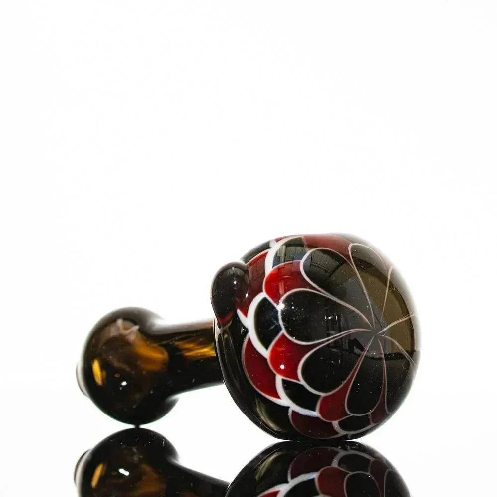 Hand-blown glass pipe with red, black, and white floral design on amber stem, reflective surface