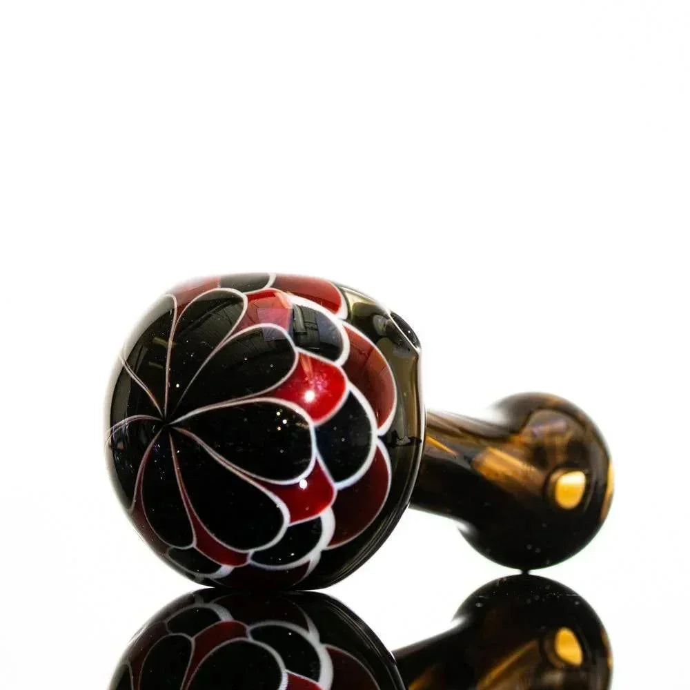 Handblown glass pipe with black, red, and white floral design on reflective surface