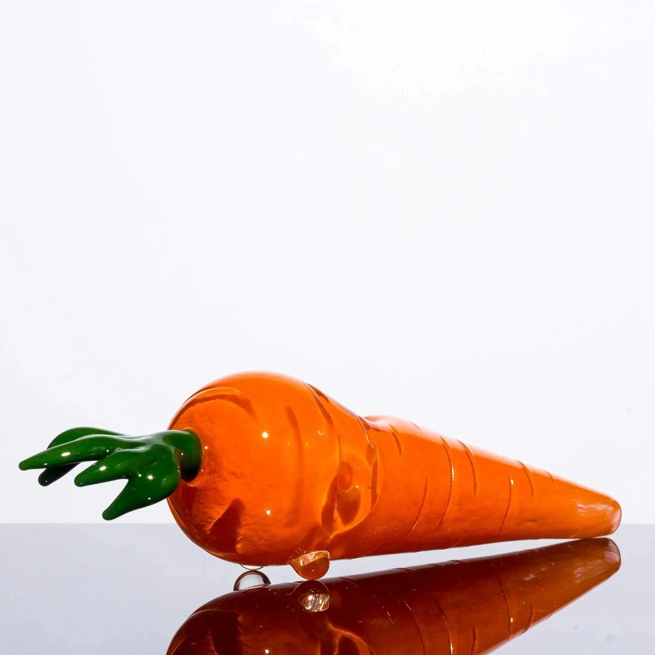 Handblown glass carrot pipe with green leaf top, vibrant orange body, and reflective surface