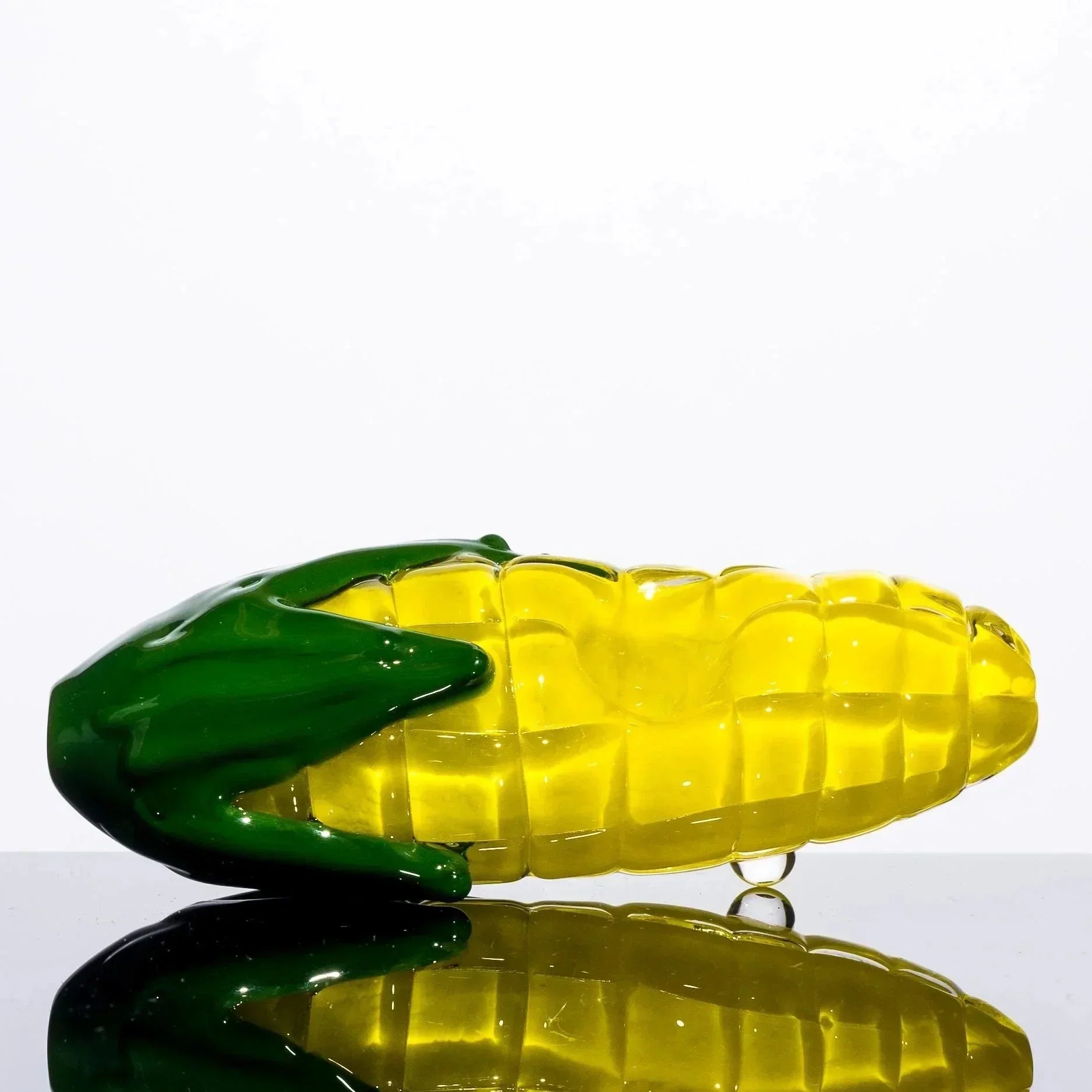 Hand-blown glass corn cob pipe with green husk, vibrant yellow kernels, reflective surface