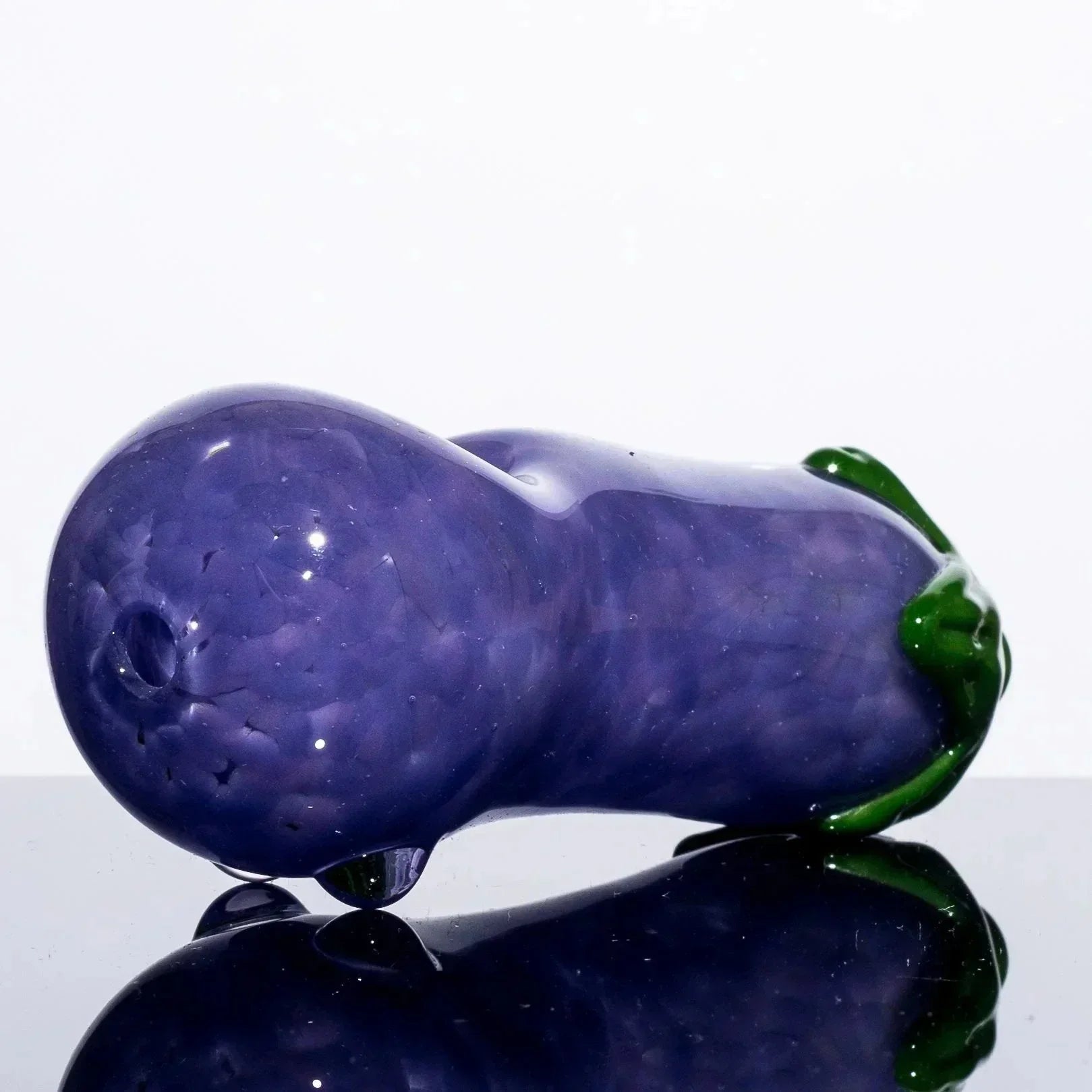 Purple glass pipe shaped like an eggplant with green stem, glossy finish, reflective surface