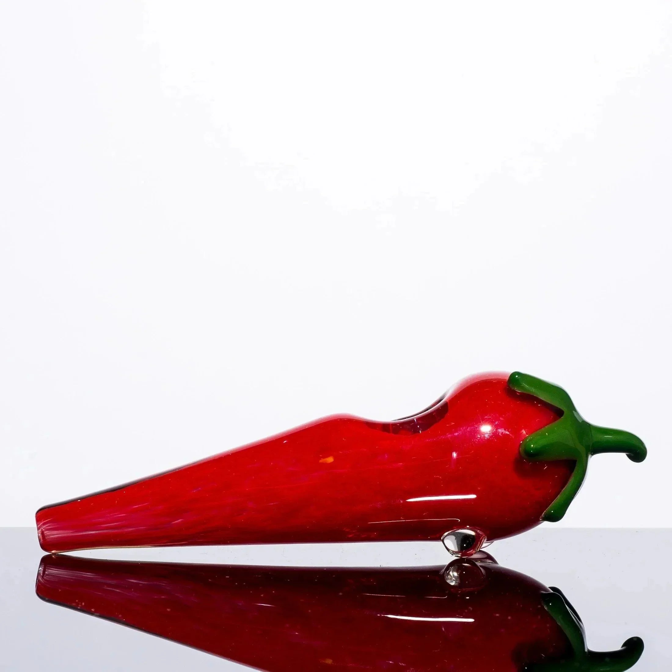 Red chili pepper-shaped glass pipe with green stem, reflective surface