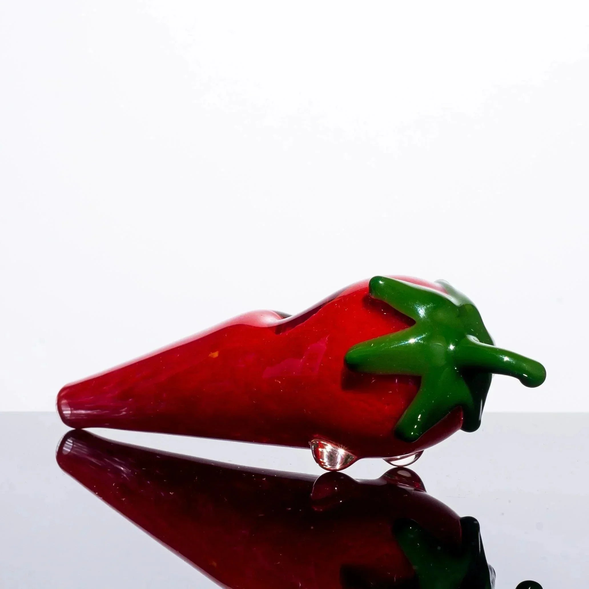 Red chili pepper-shaped glass pipe with green stem, reflective surface