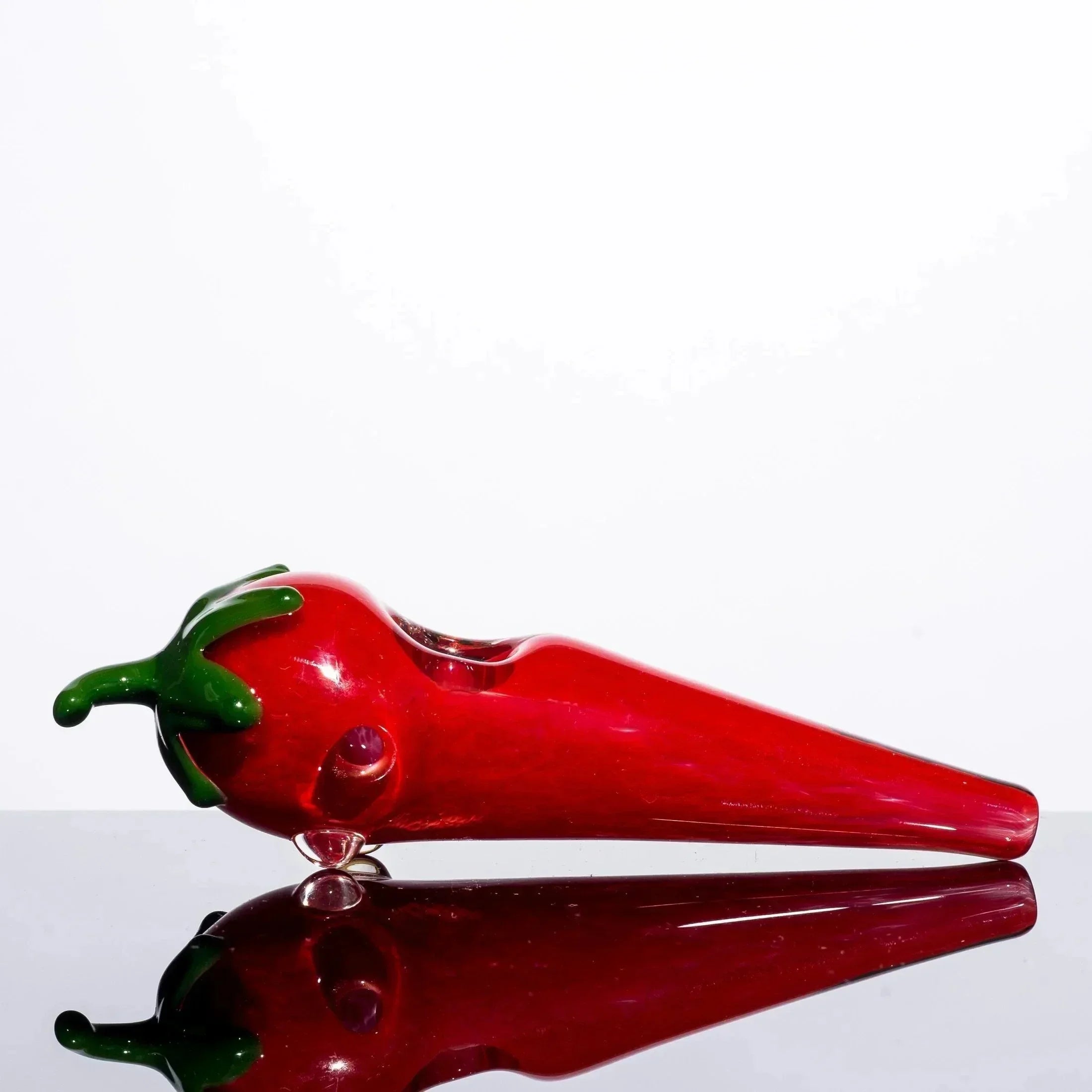 Red chili pepper shaped glass pipe with green stem, reflective surface, heady glass art