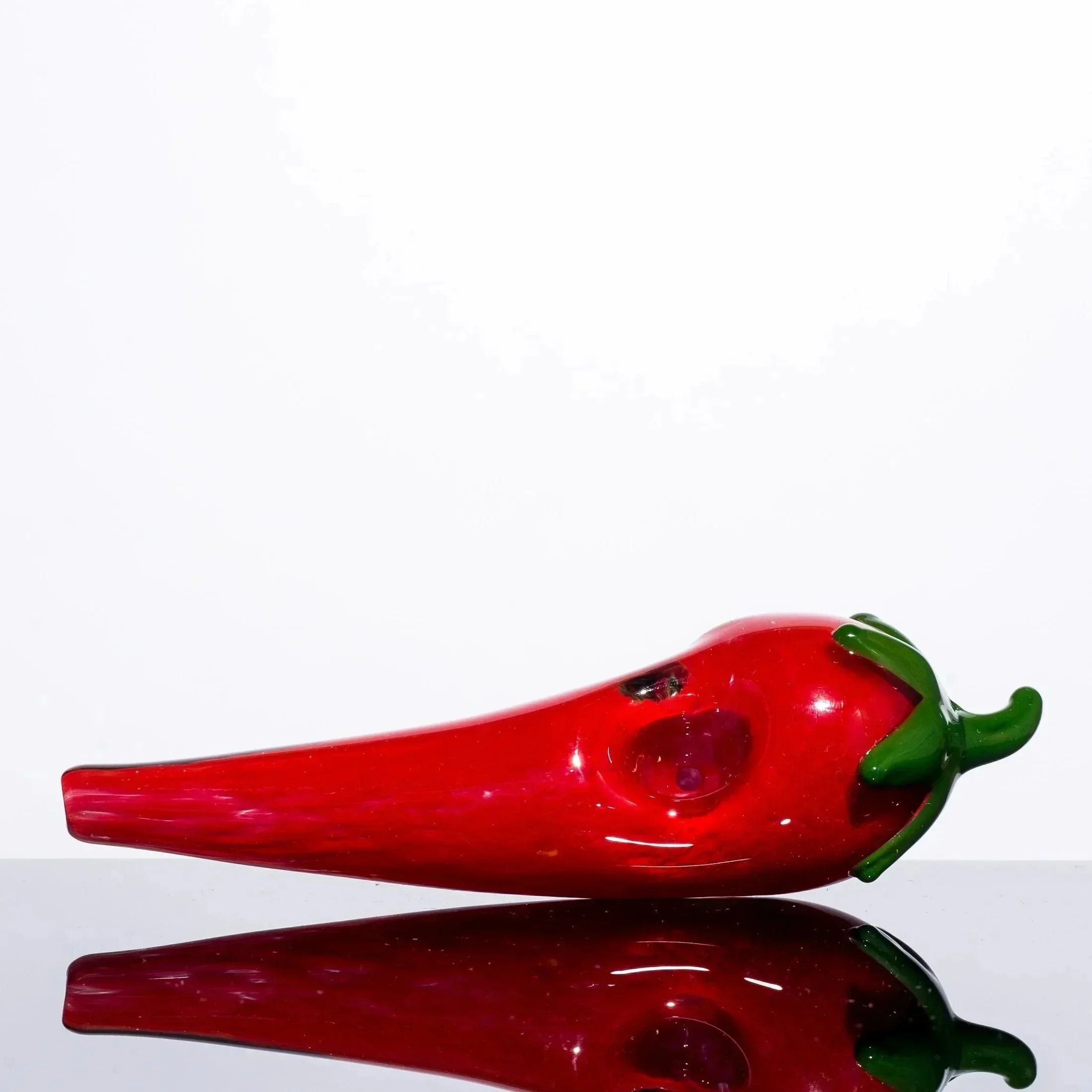 Red chili pepper-shaped glass pipe with green stem, glossy finish, on reflective surface