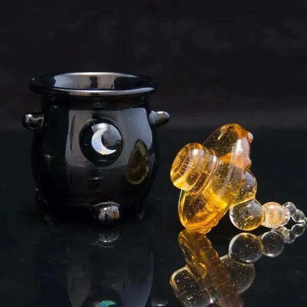 Black glass pipe with moon design beside amber glass bubbler on reflective surface