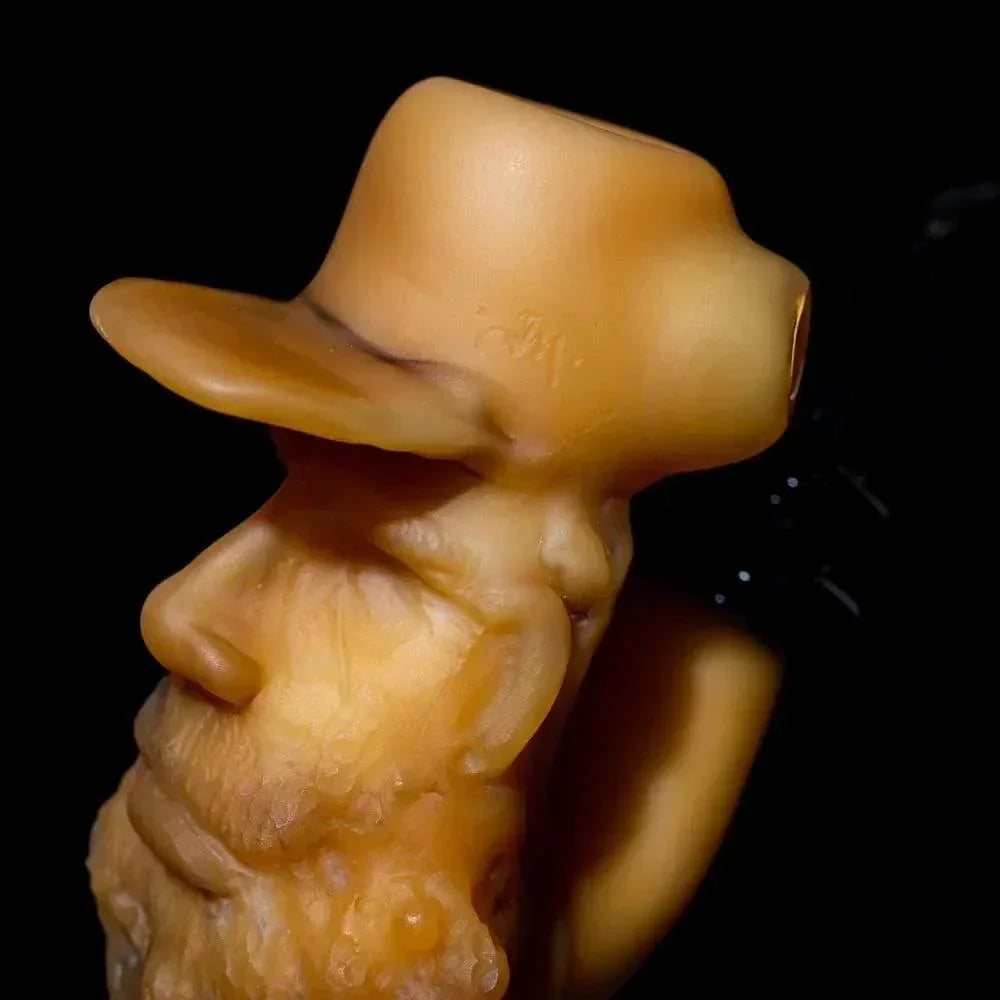 Handcrafted glass pipe shaped like an old man's face with a hat, close-up on black background.