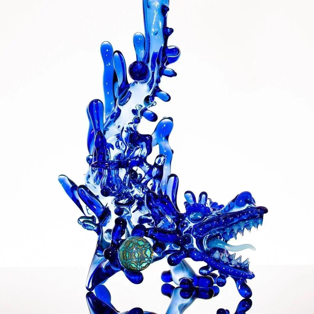 Vibrant blue heady glass dragon sculpture with intricate details and a green orb accent