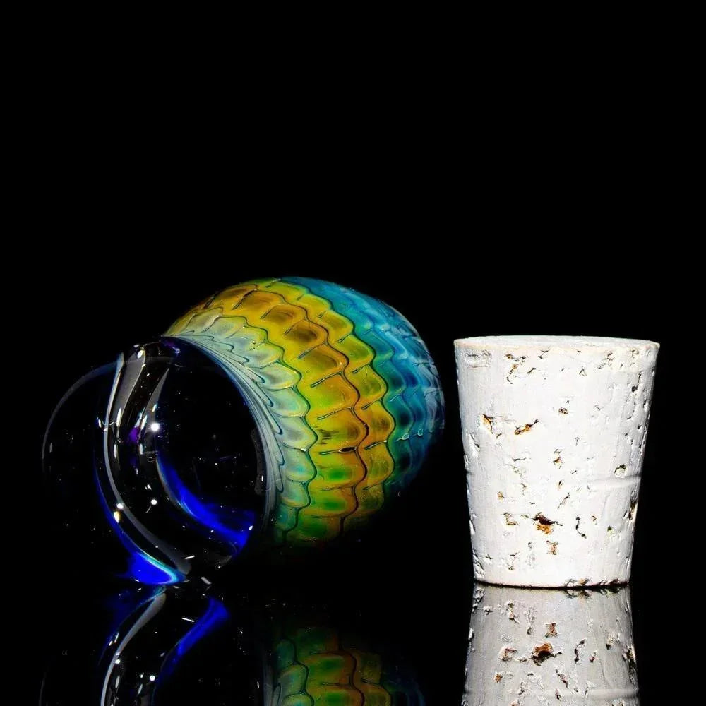 Mini glass jar with cobalt blue and fume pattern next to white cork stopper on black background