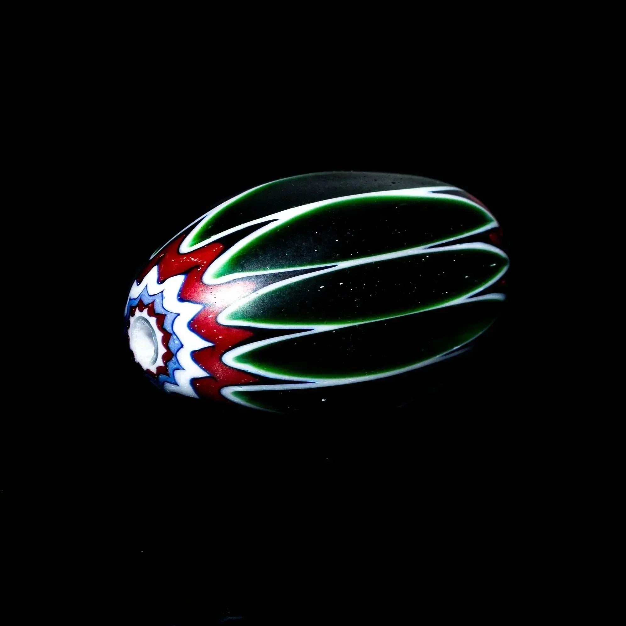 Handmade marquise glass bead with green, white, and red chevron pattern on black background