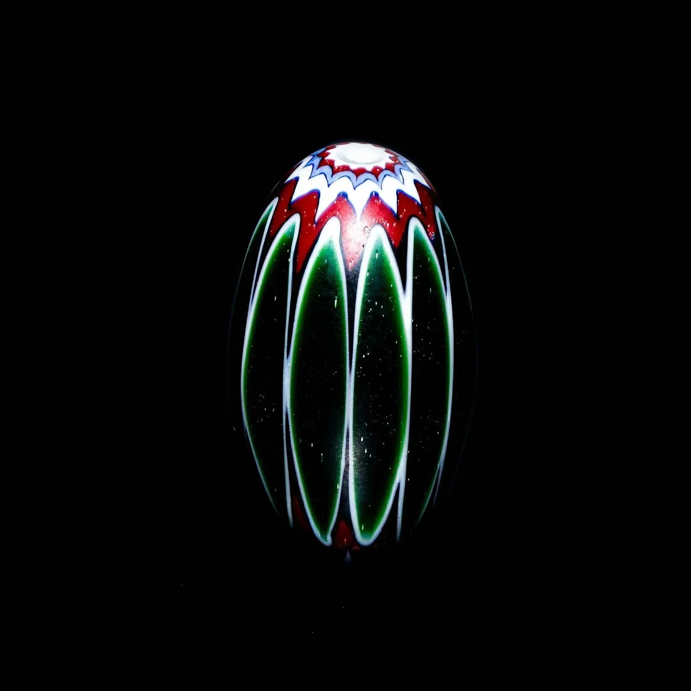 Large marquise glass bead with green, white chevron design and red accents on black background