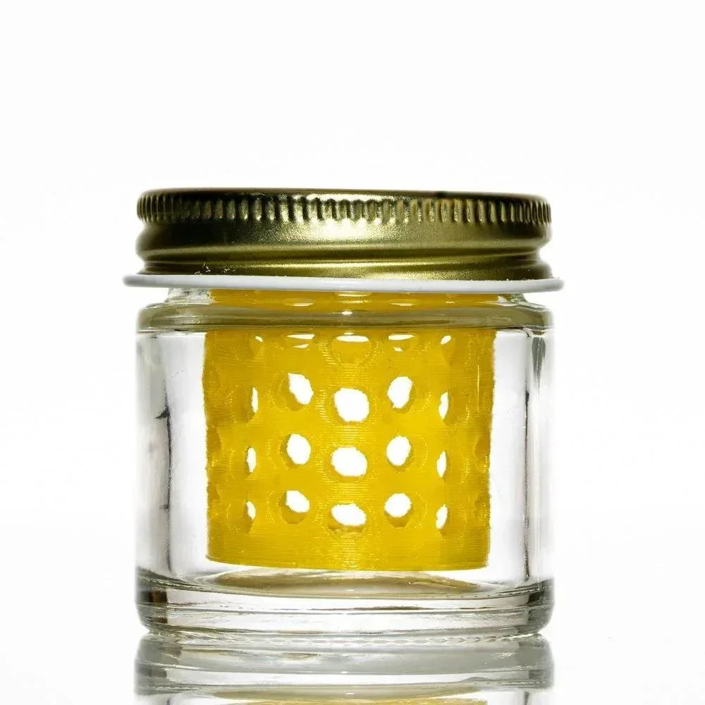 Clear glass jar with metal lid containing a yellow, perforated insert on white background.