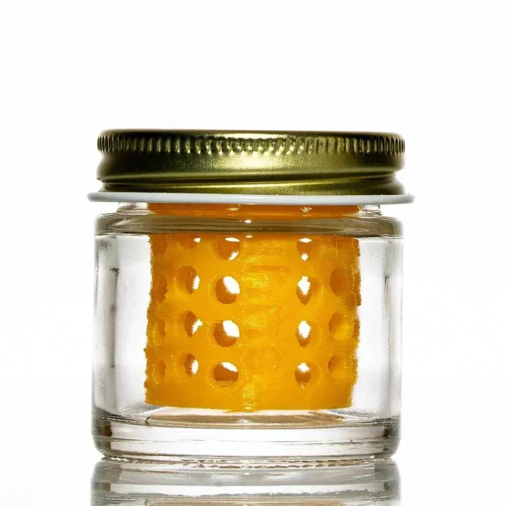 Glass jar with gold lid containing yellow perforated insert, clean background