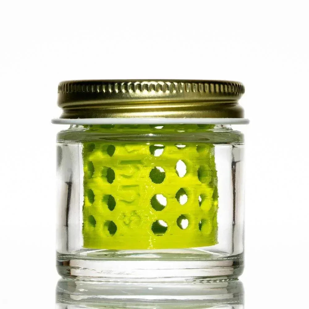 Glass jar with gold lid containing a neon green perforated insert, isolated on white background